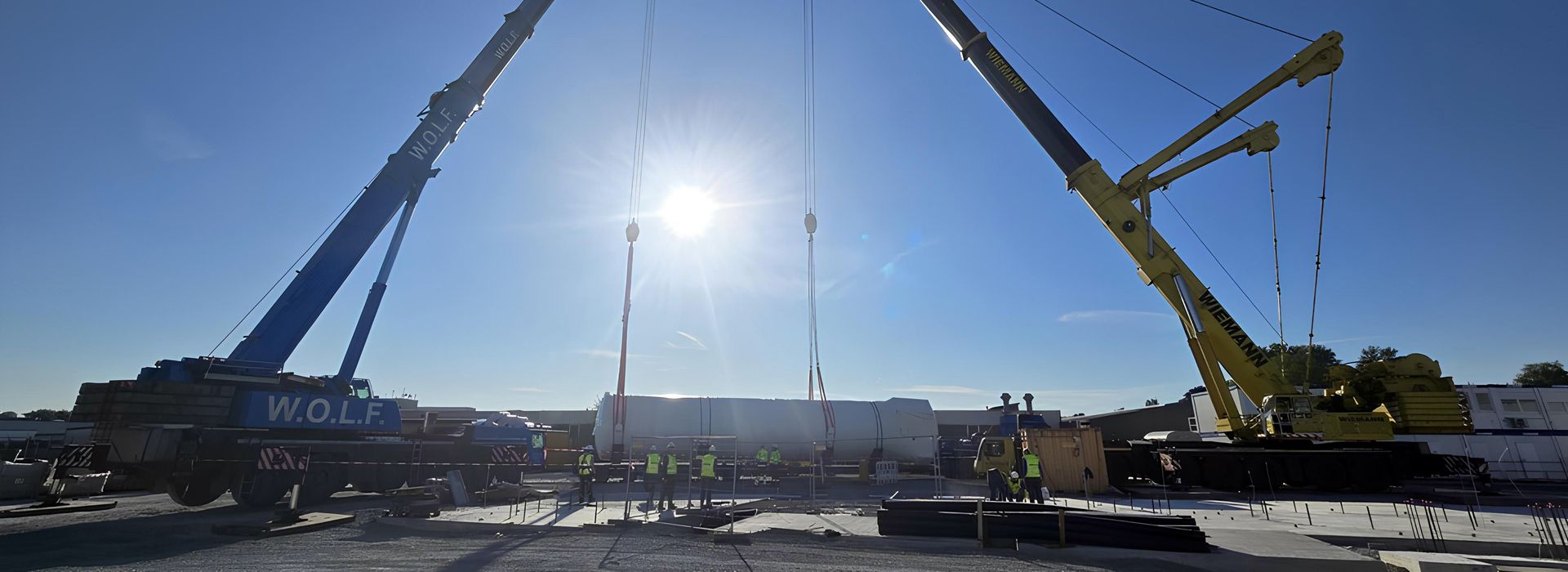 Zwei große Kräne auf einer Baustelle vor strahlend blauem Himmel mit tiefstehender Sonne.
